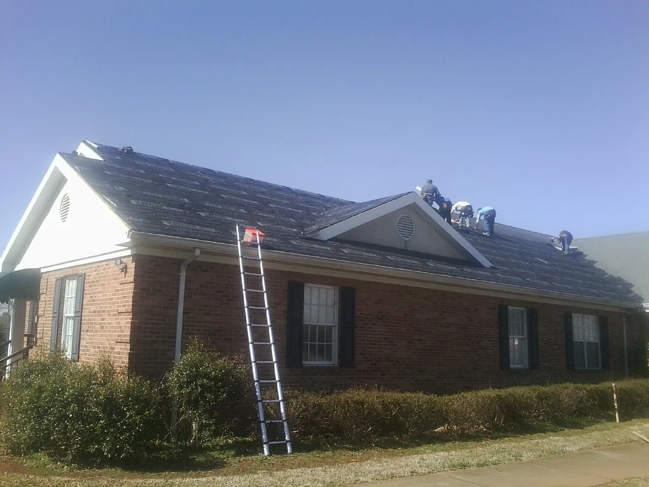 Crew tearing shingles off a brick ranch roof with a ladder set — Emergency Roof Repair work by our crew in La Fayette
