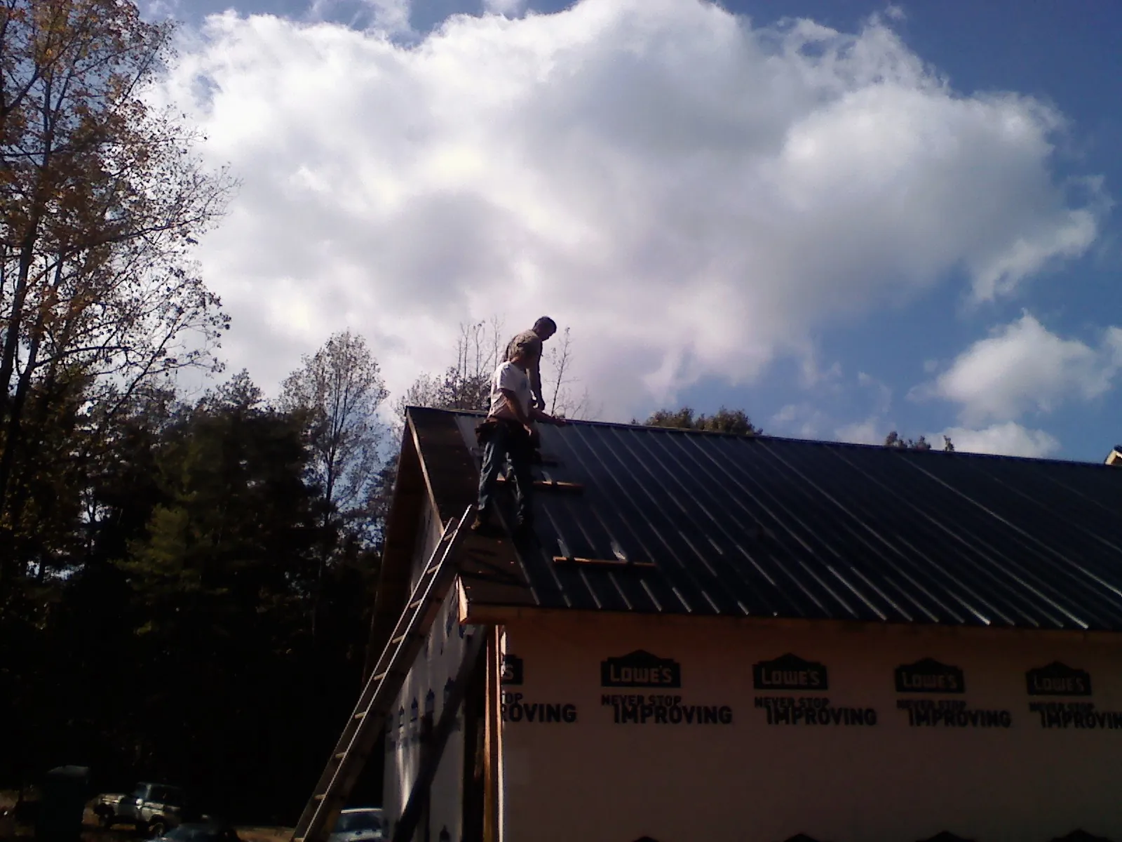 Roofer fastening dark metal panels high against a cloudy sky, from a Roof Inspection job in La Fayette